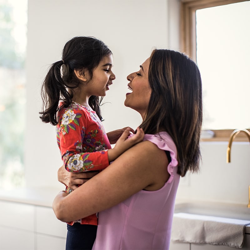 A woman holding her daughter in her arms and both of them are smiling.