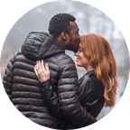 A man and a woman are embracing each other while he kisses her forehead and she smiles.