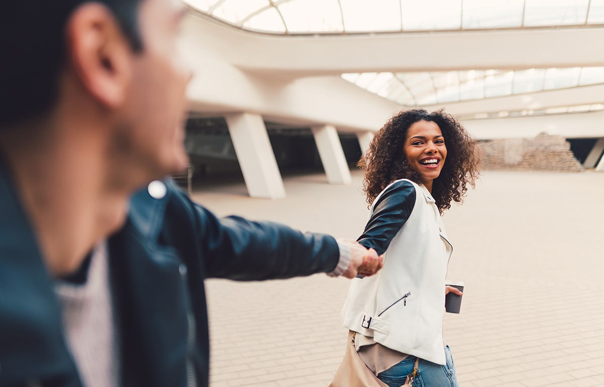 Male and female chefs smile at each other while preparing pizzas in a kitchen.